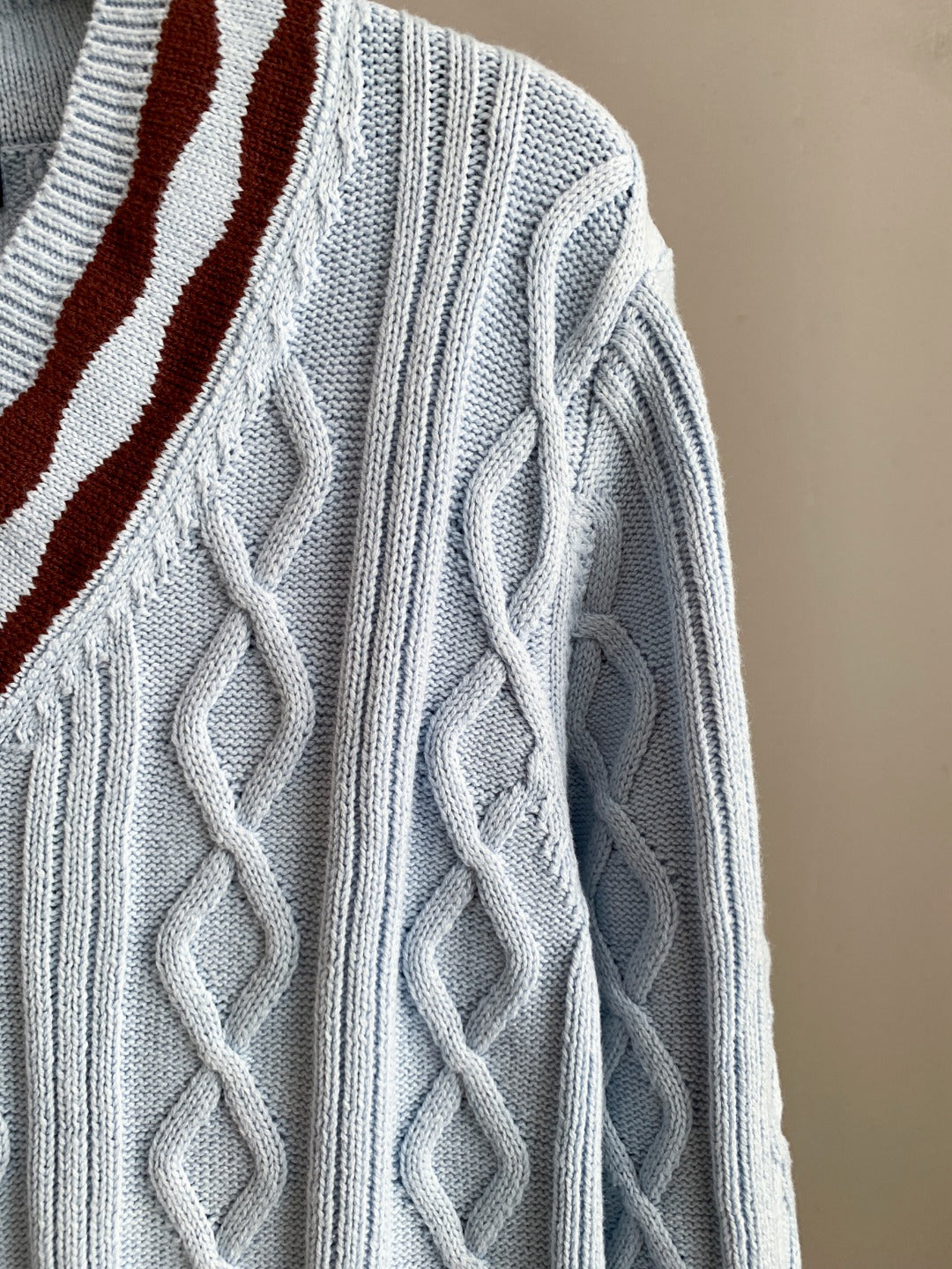 Light blue long-sleeve knit sweater with raised cable texture and striped V detail