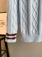 Light blue cable-knit sweater sleeve with dark red and white striped cuff