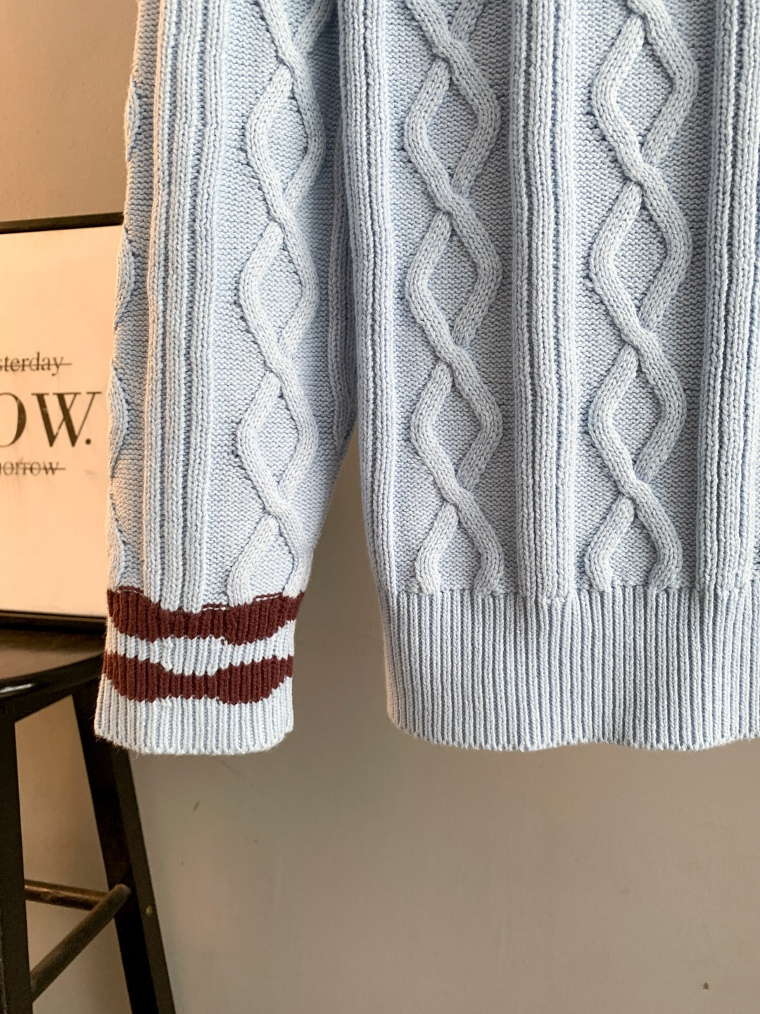 Light blue cable-knit sweater sleeve with dark red and white striped cuff