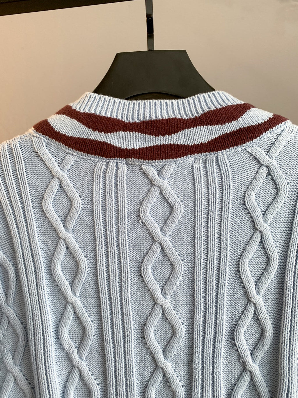 Back view of long cable-knit sweater in light blue with striped collar detail