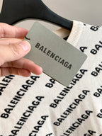 Cream knit sweater with black BALENCIAGA logo pattern; clothing tag held near collar