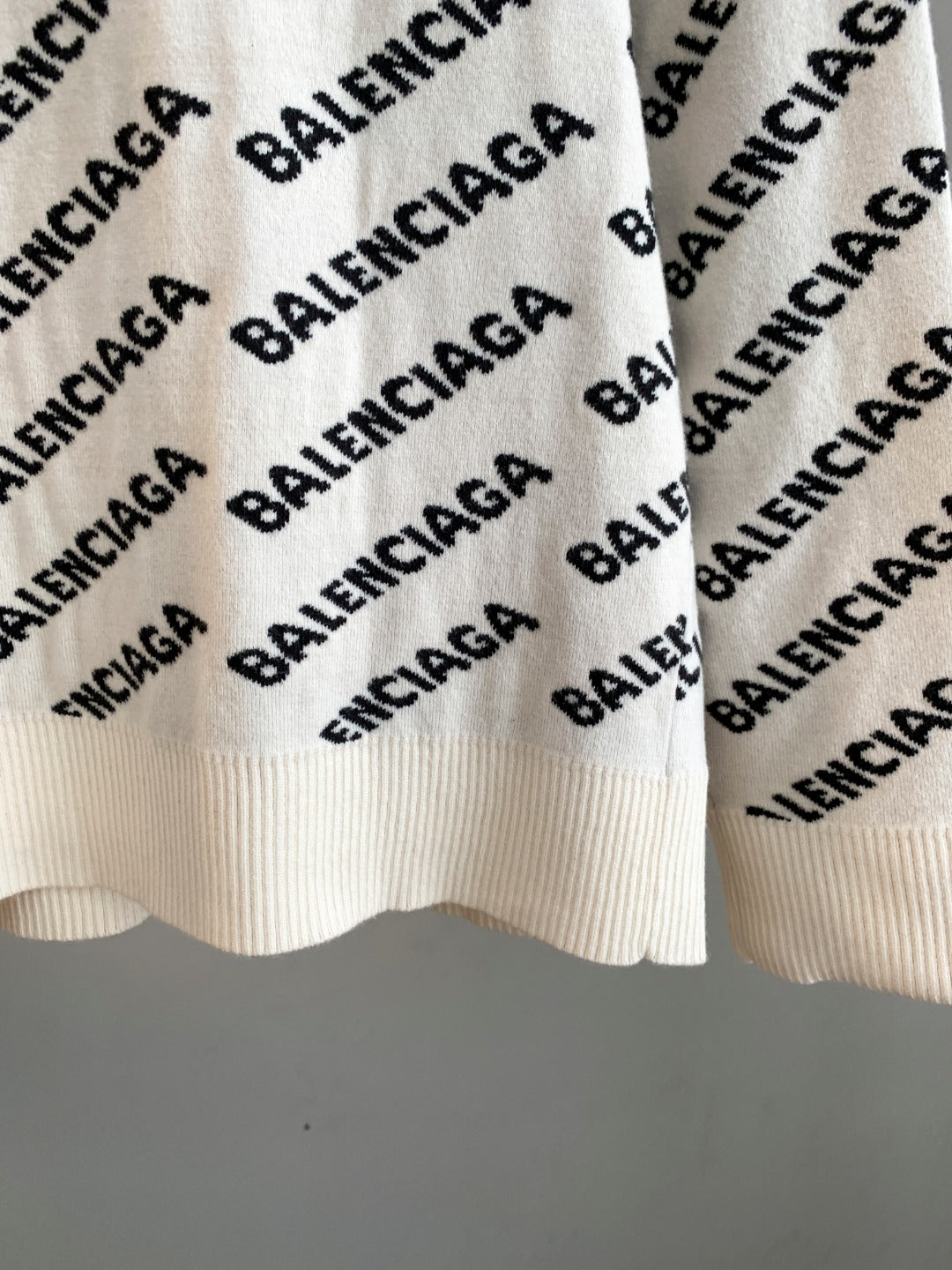 Cream knit sweater hem with black BALENCIAGA logo pattern and ribbed bottom edge