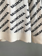 Cream knit sweater hem with repeating black Balenciaga logo pattern and ribbed bottom
