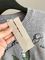 Dior grey knit sweater with hanging brand tag held near neckline