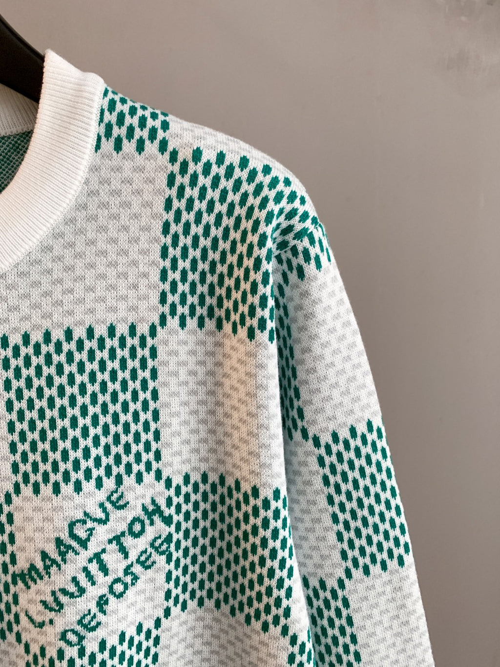 Sweater sleeve with green-and-white check knit squares and logo print