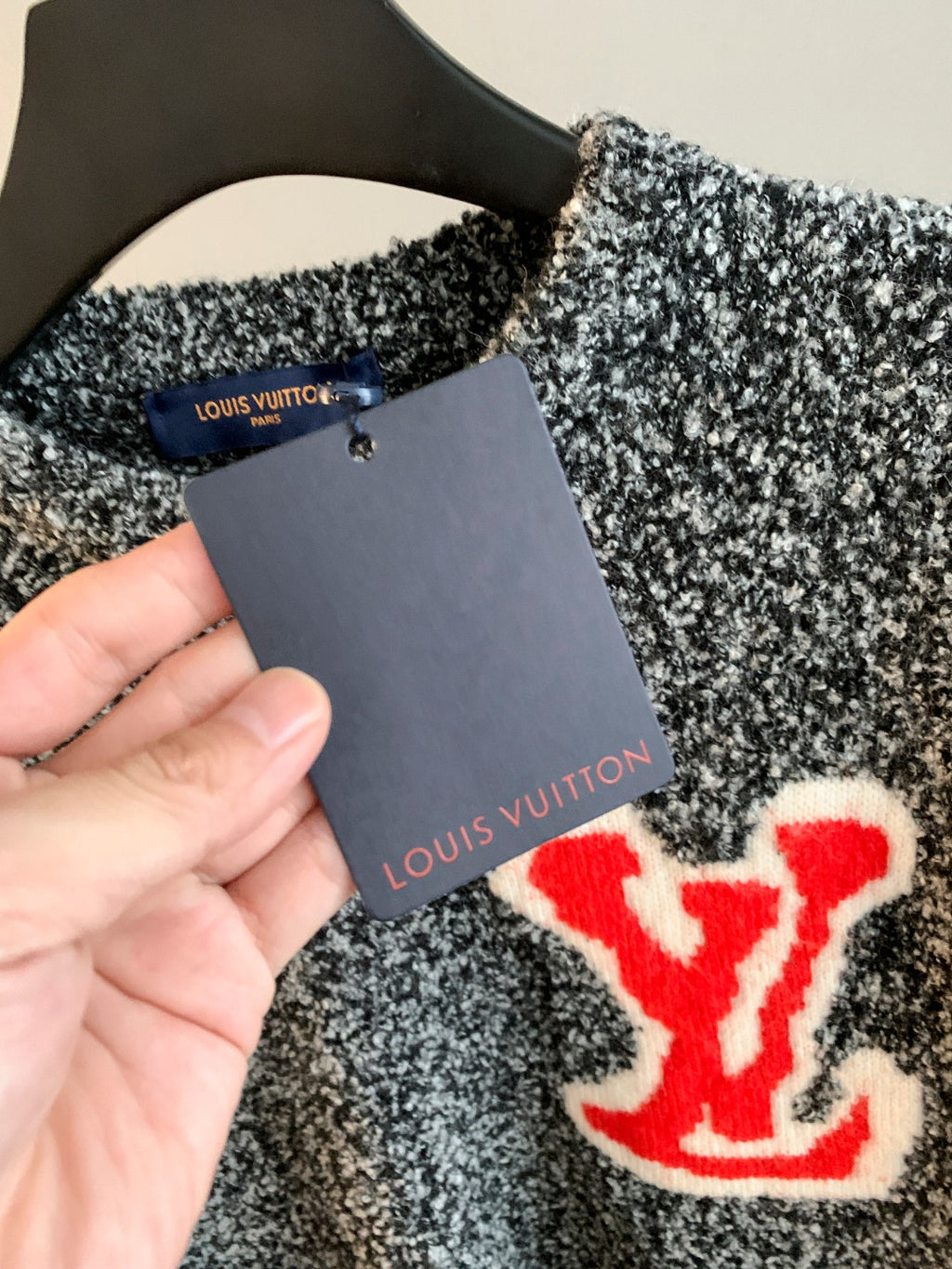 Speckled knit sweater with red logo patch and attached price tag