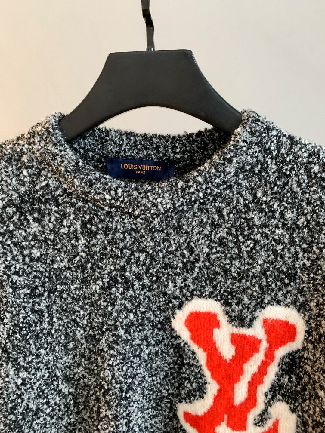 Speckled knit sweater with crew neck and red logo patch, close-up on chest