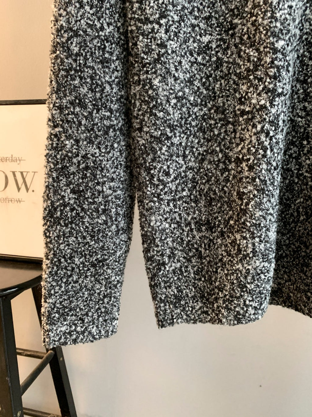 Speckled black and white knit sweater on hanger, long sleeves and hem visible