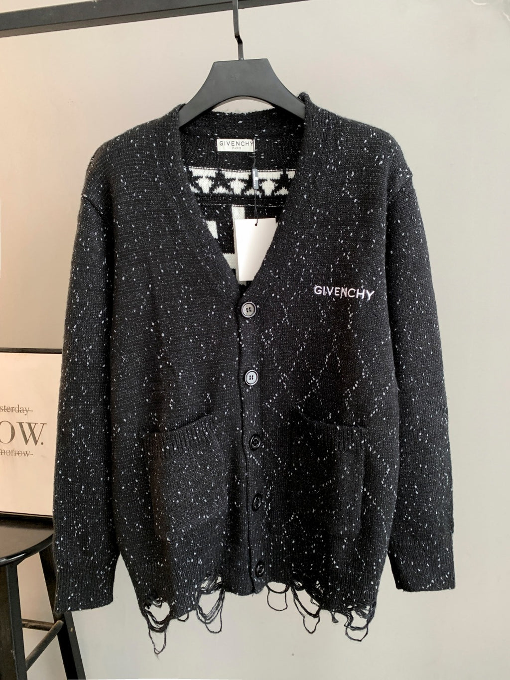 Black speckled cardigan with button front, V-neck, and patterned knit hem fringe.