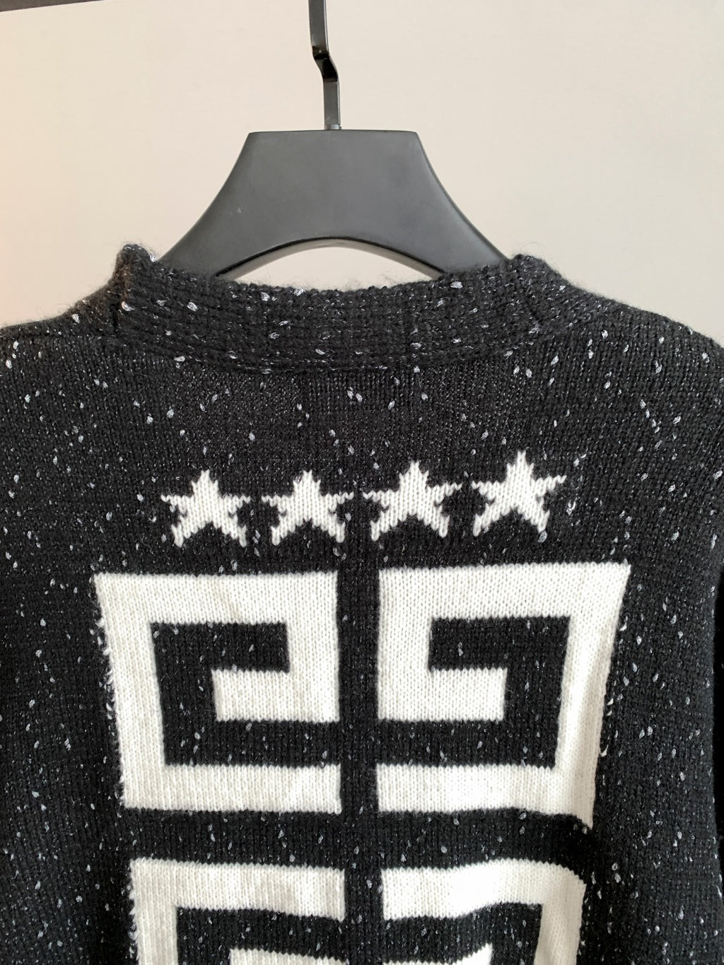 Black cardigan back close-up with white geometric logo and star motif.