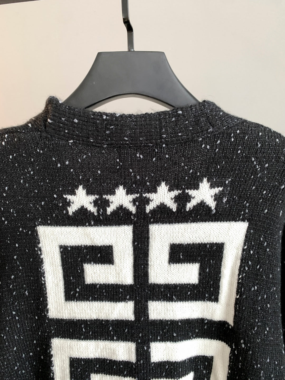 Black cardigan back close-up with white geometric logo and star motif.