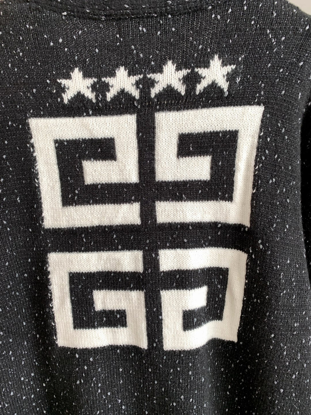 Black cardigan close-up with white geometric logo and star row at upper back.