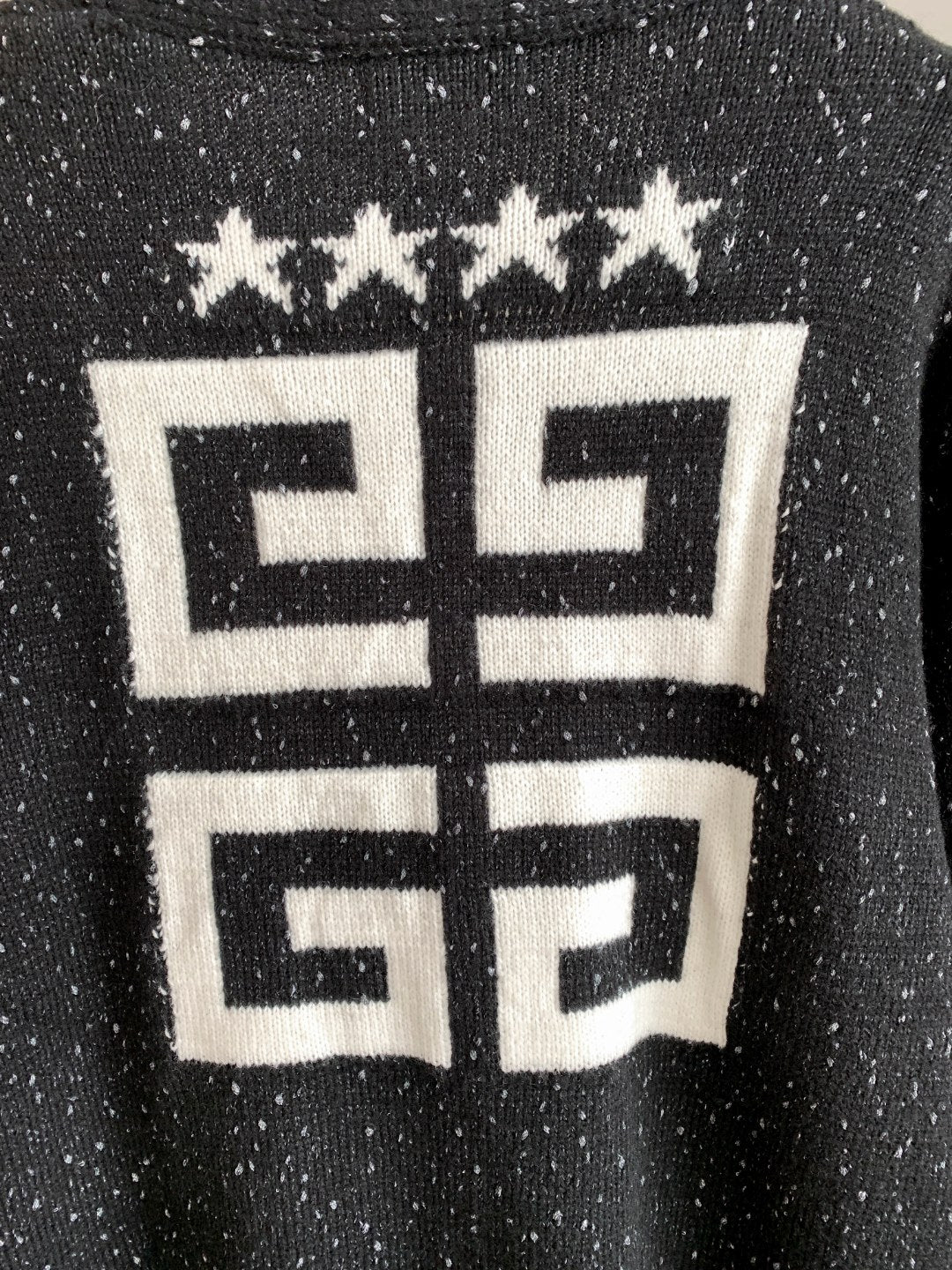Black cardigan close-up with white geometric logo and star row at upper back.