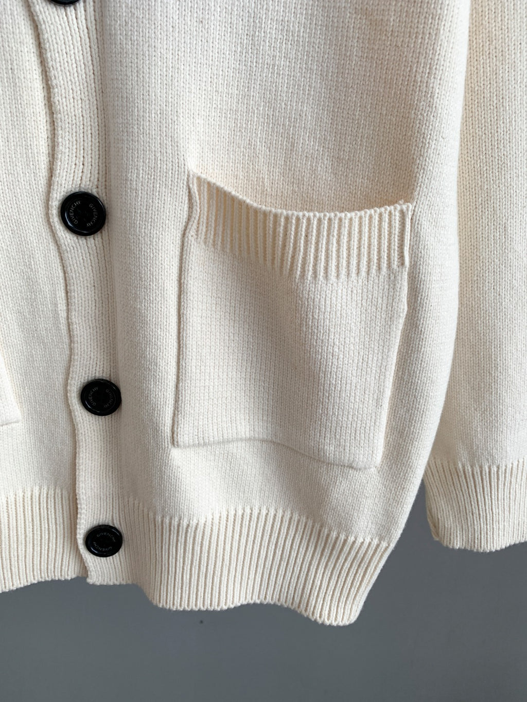 White knit cardigan front pocket with ribbed hem and black button detail