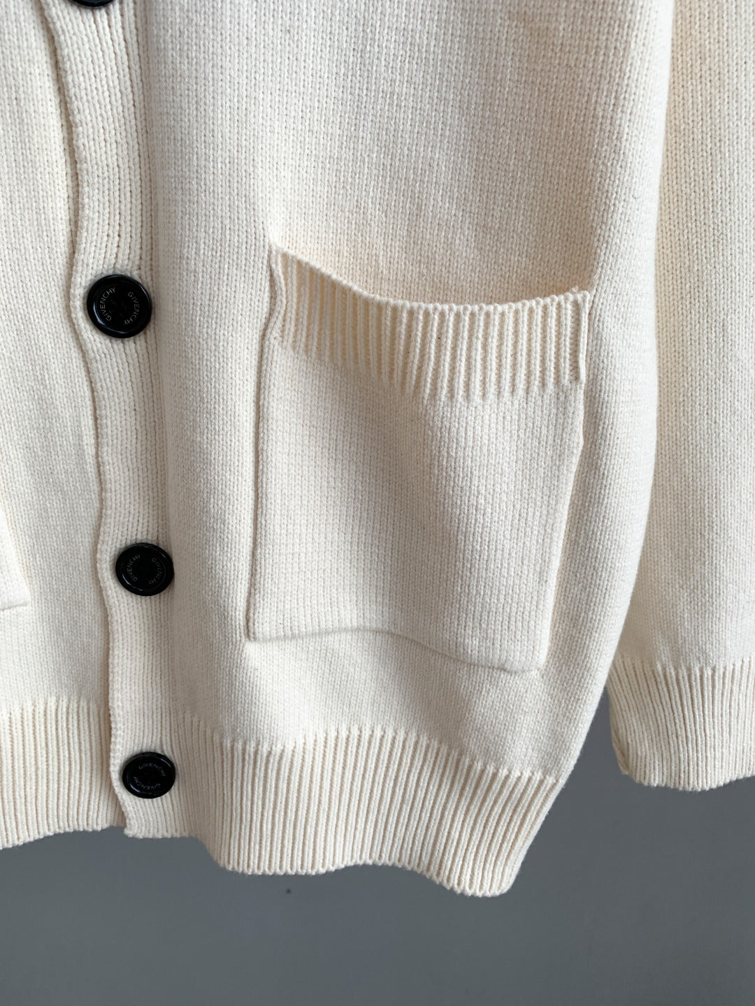 White knit cardigan front pocket with ribbed hem and black button detail