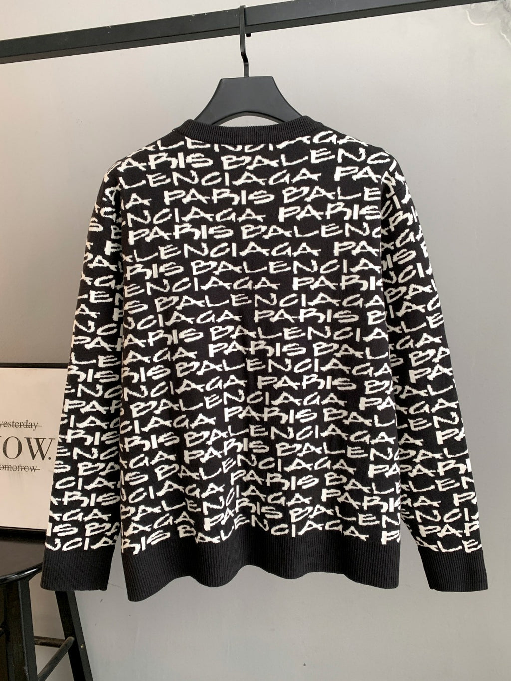Black long-sleeve sweater with white repeating logo text; ribbed hem and crew neck