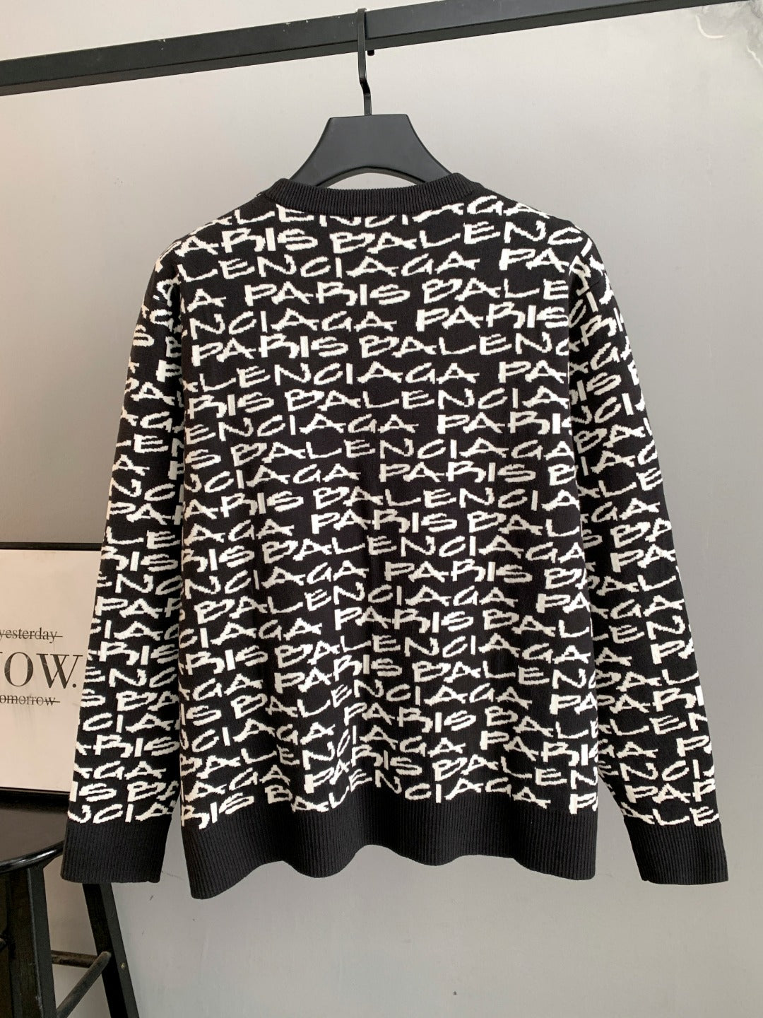 Black long-sleeve sweater with white repeating logo text; ribbed hem and crew neck