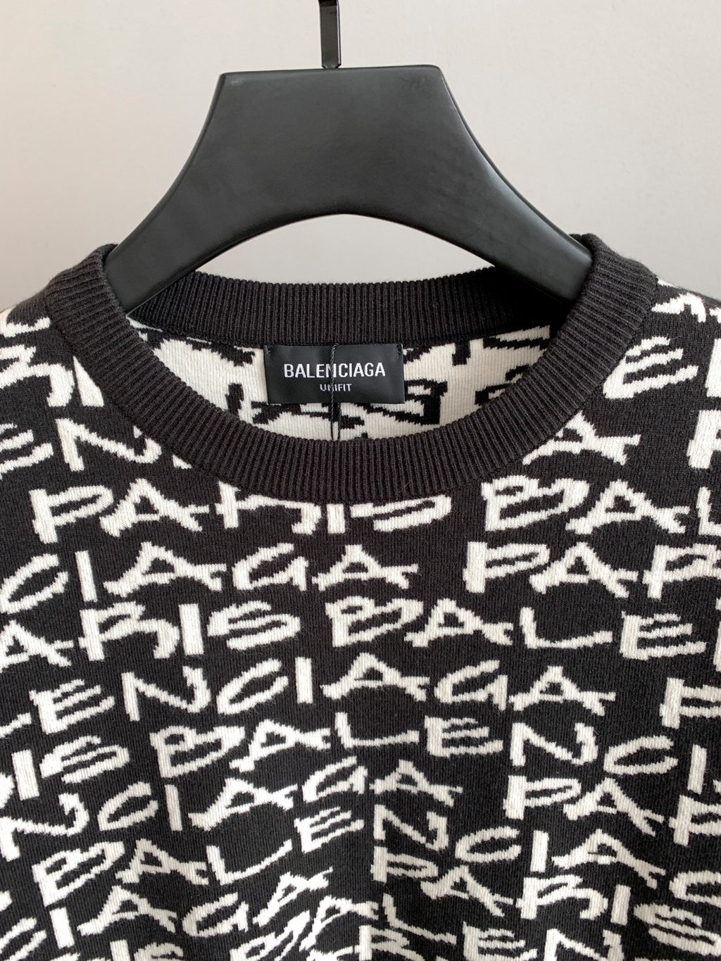 Close-up of black sweater neckline with ribbed crew collar and white repeating logo text