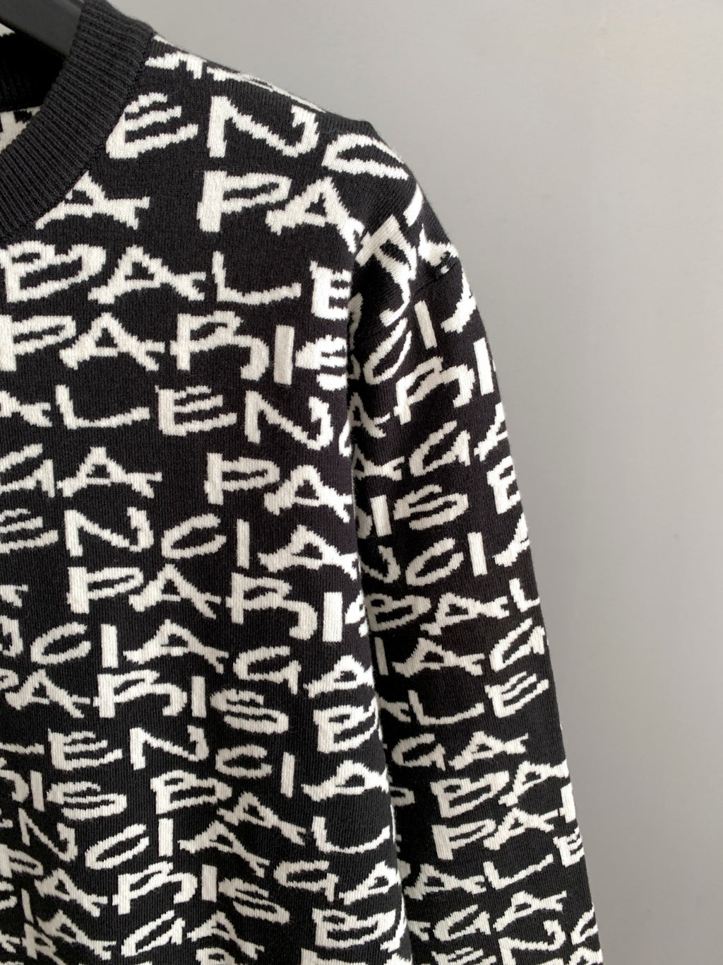 Side view of black long-sleeve sweater with white repeating logo text pattern