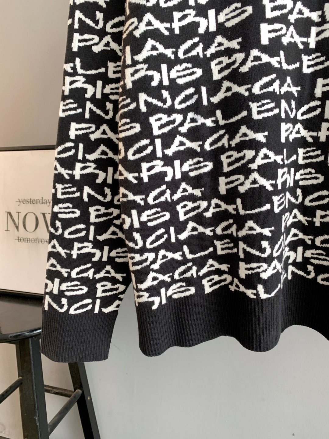 Back view of black long-sleeve sweater with white repeating logo text; ribbed hem