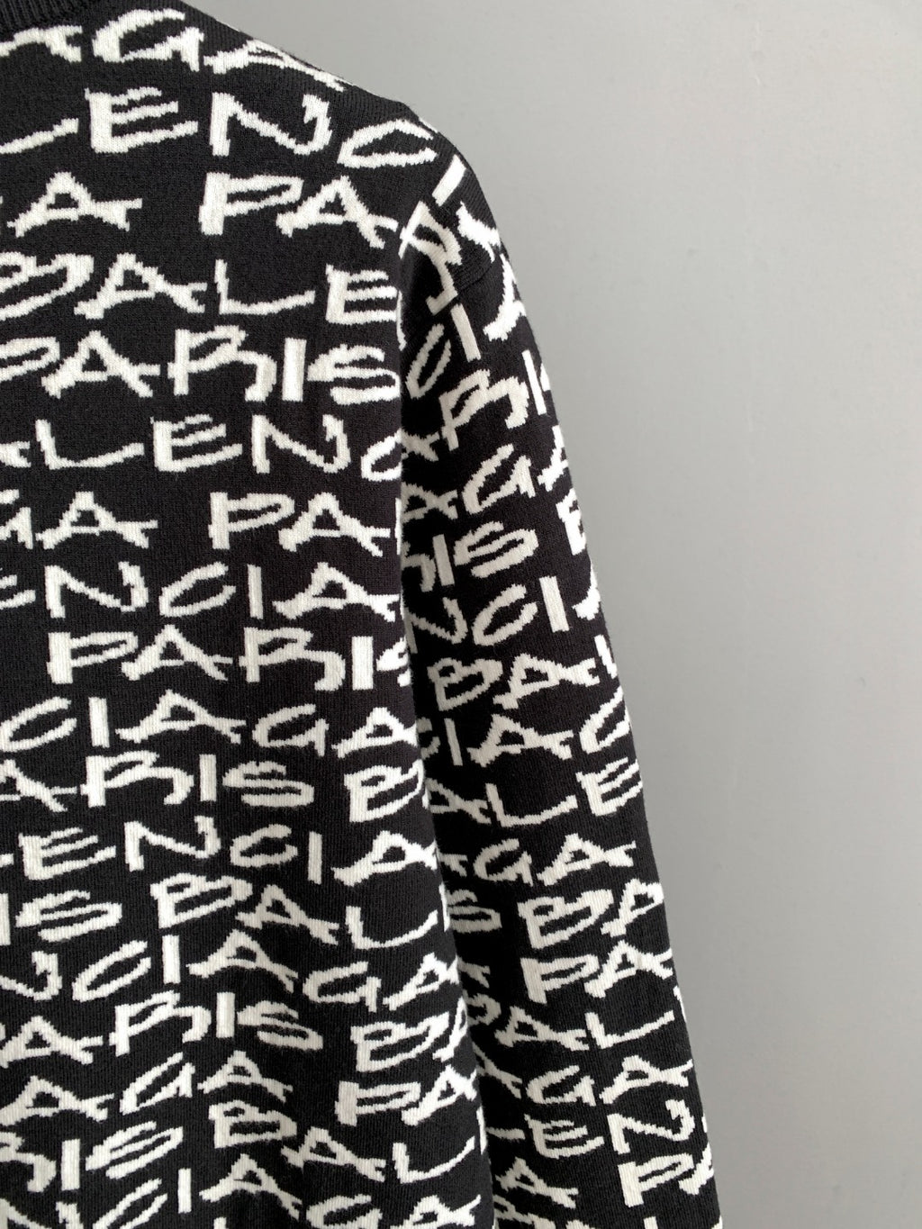 Sleeve side view of black long-sleeve sweater with white repeating logo text
