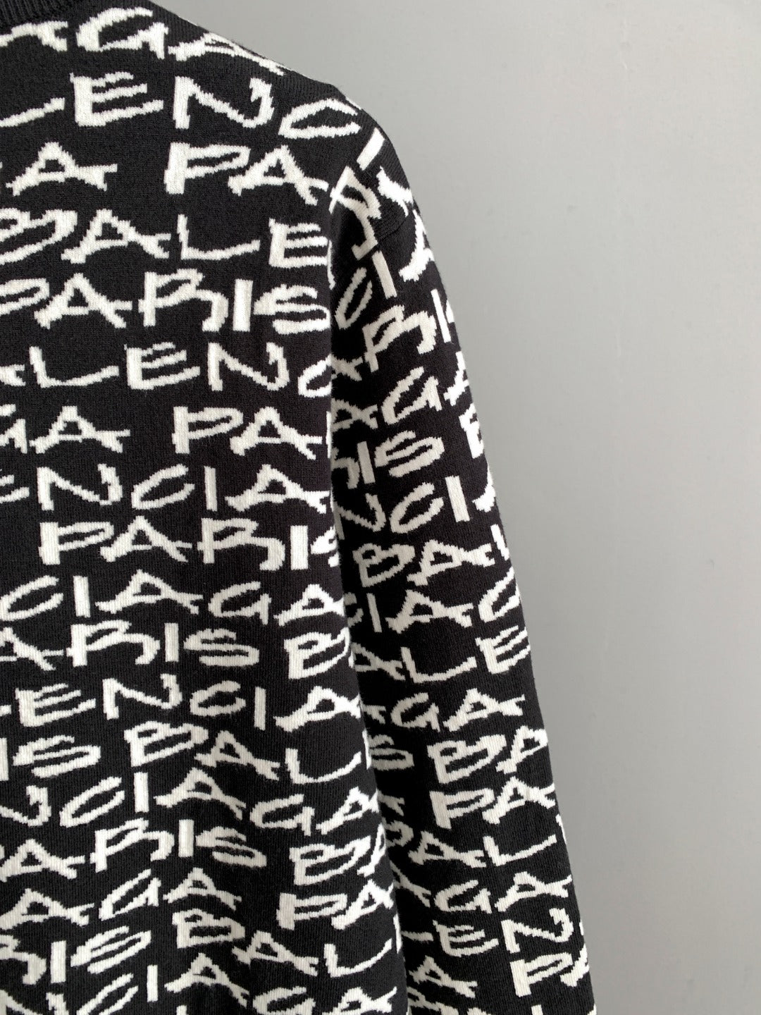 Sleeve side view of black long-sleeve sweater with white repeating logo text