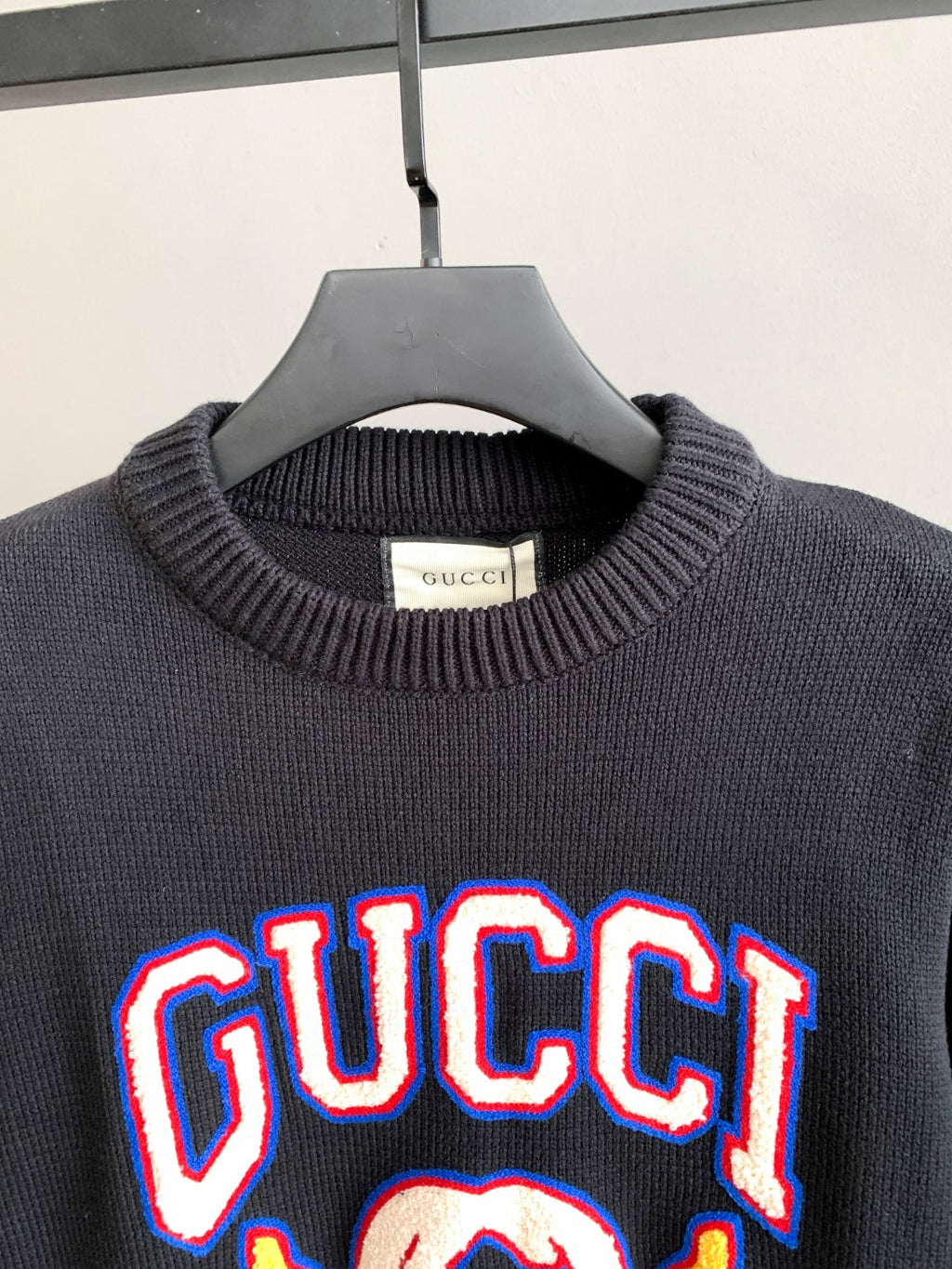 Gucci knit sweater close-up at neckline with “GUCCI” logo graphic on front