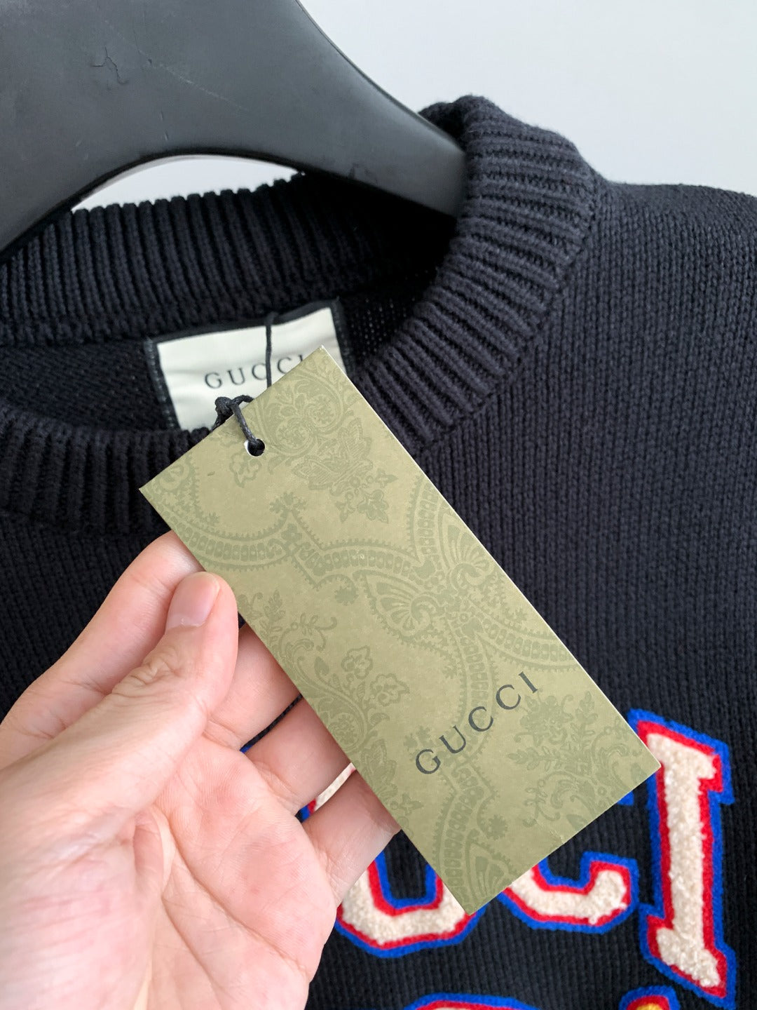 Gucci knit sweater tag held in hand, shown on dark knit fabric