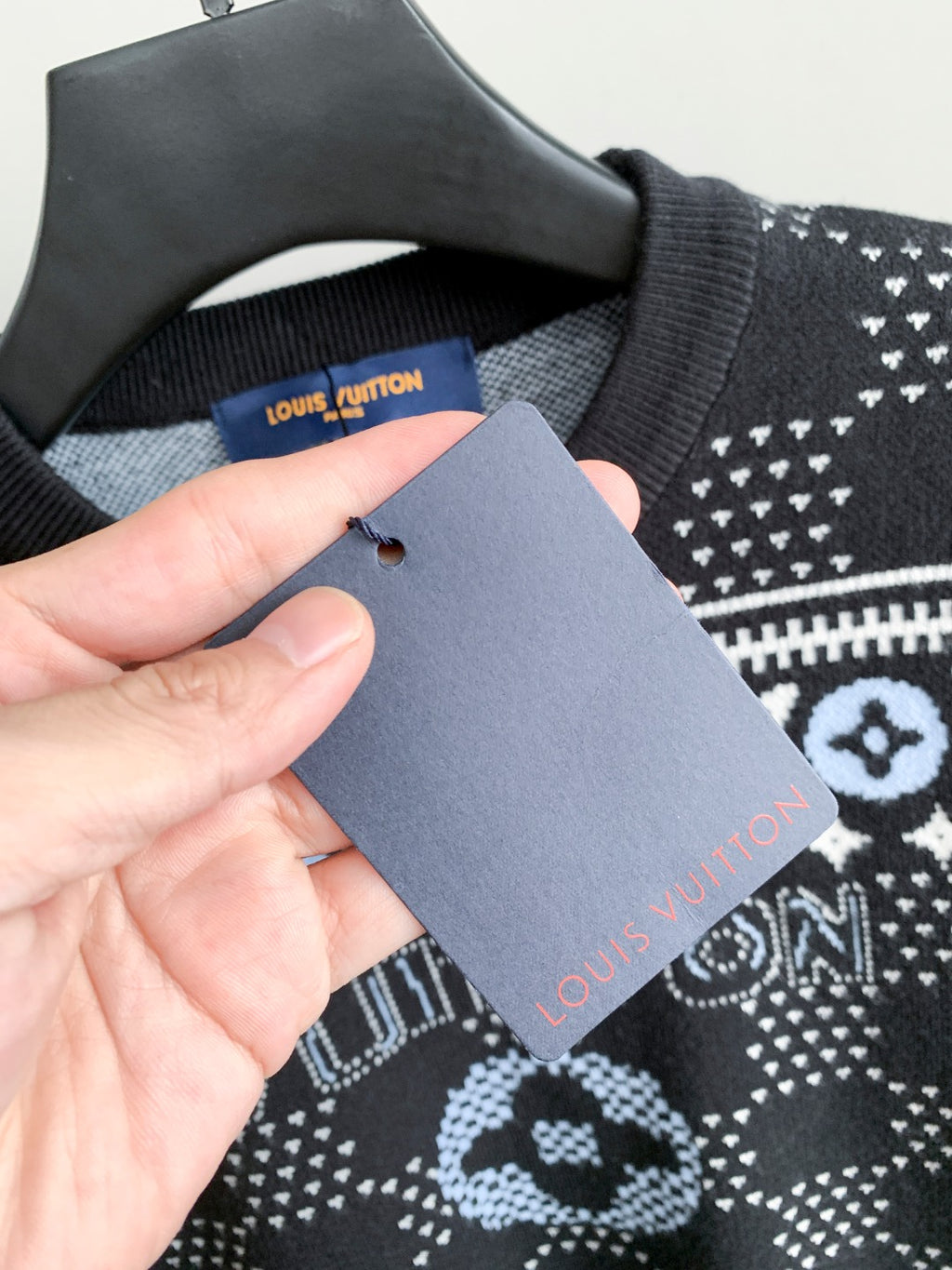 Tag on crew-neck knit sweater collar with dark fabric and white monogram motifs
