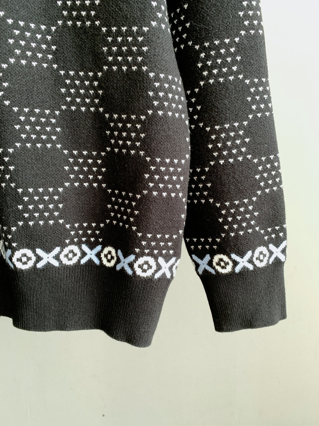 Lower sleeve view of long-sleeve knit sweater with dark base and white motif stripes