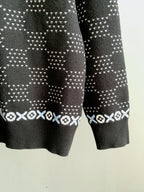 Lower sleeve view of long-sleeve knit sweater with dark base and white motif stripes