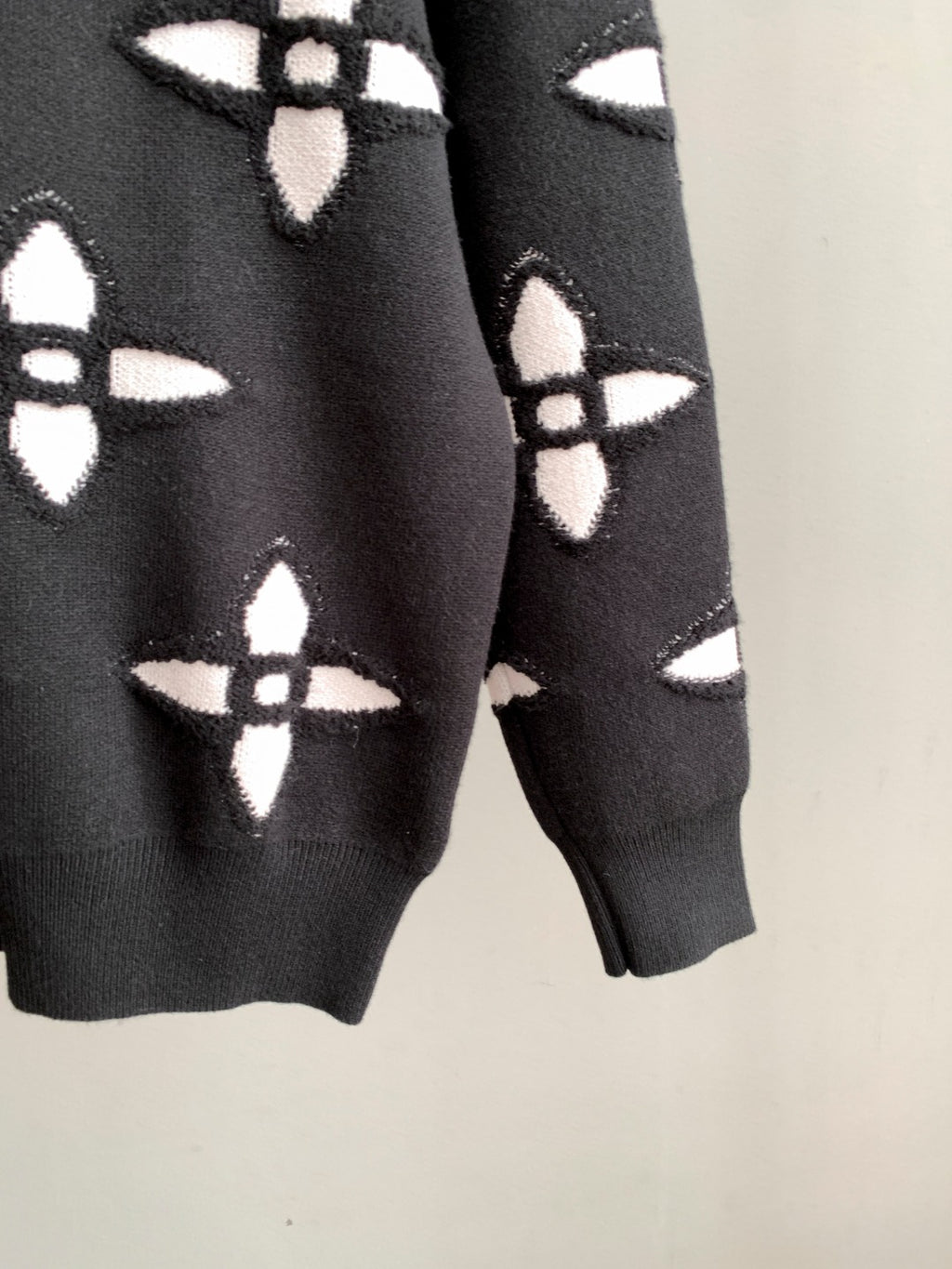 Black knit sweater sleeves with repeating white geometric monogram-style pattern