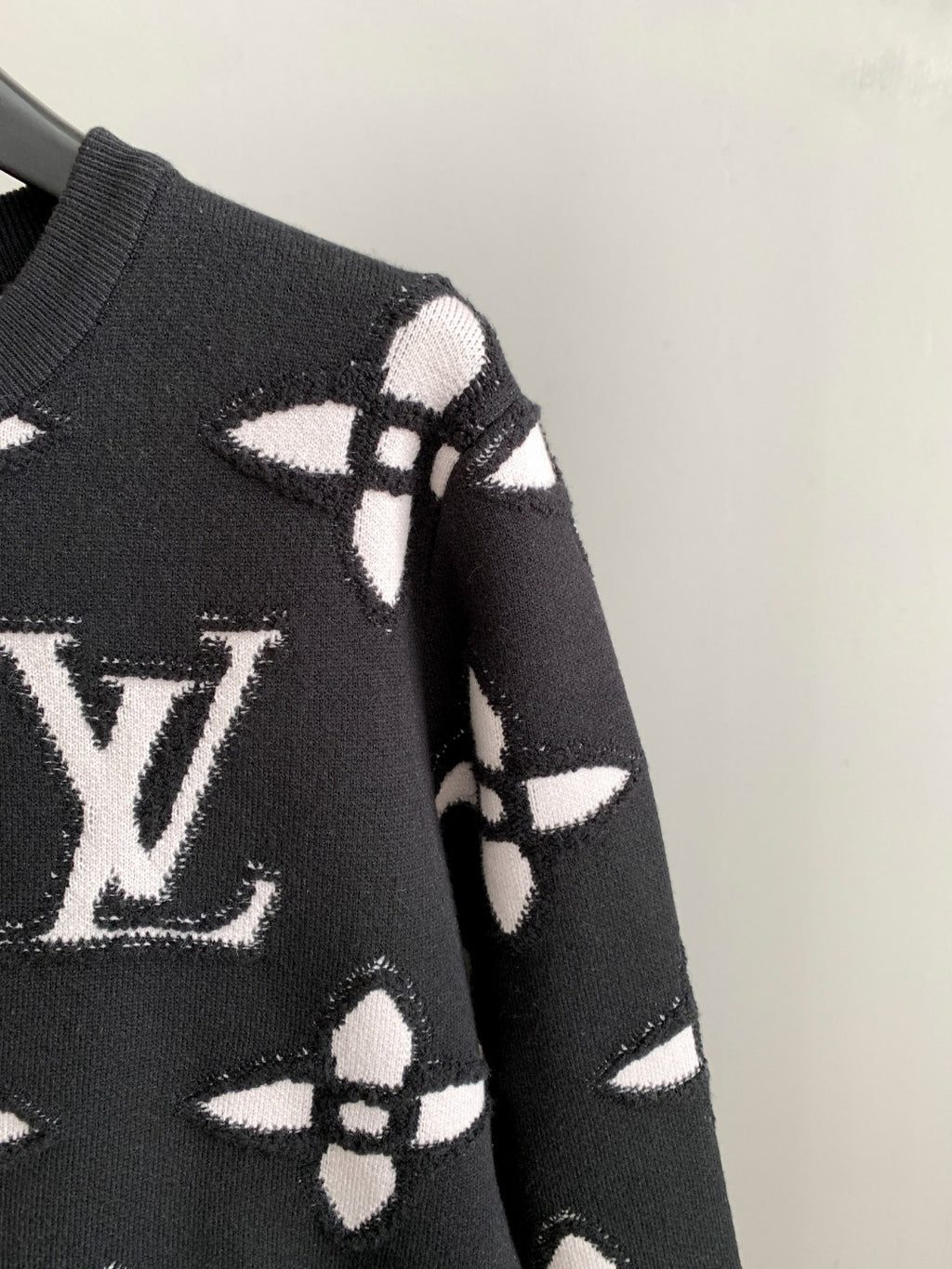 Black knit sweater shoulder and sleeve with white geometric monogram pattern
