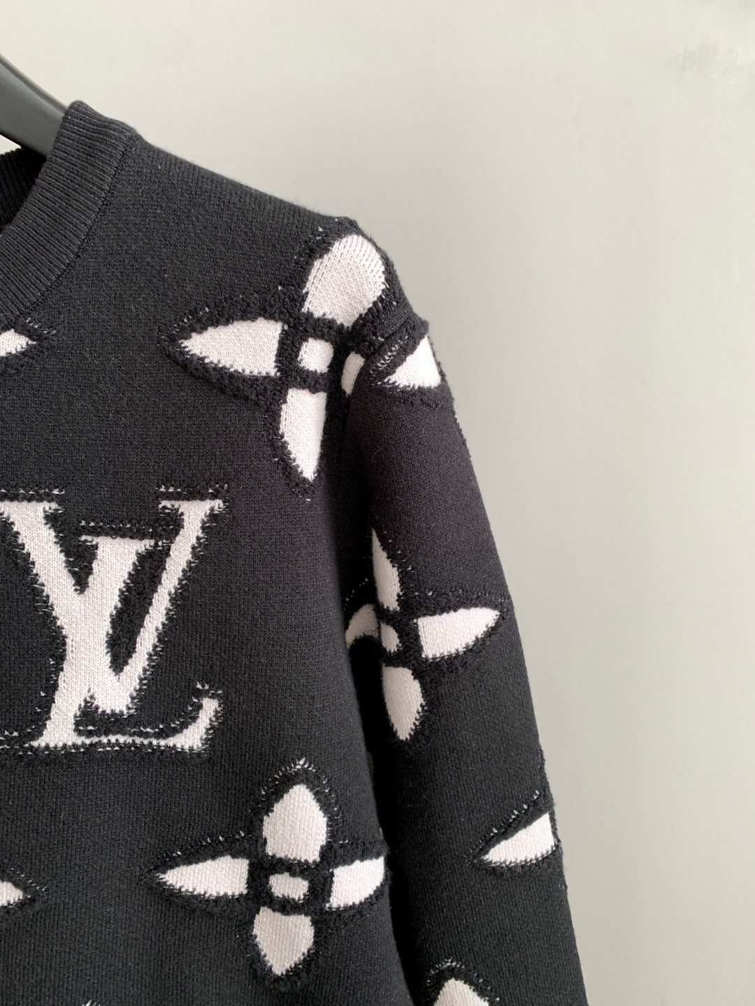 Black knit sweater shoulder and sleeve with white geometric monogram pattern