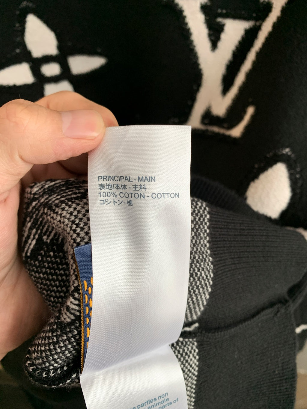Fabric care label inside black knit sweater, held against the collar