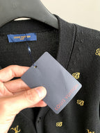 Hand holding Louis Vuitton tag on dark knit cardigan with gold monogram embroidery