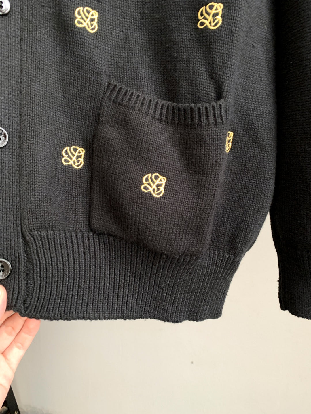 Dark knit cardigan front pocket with gold monogram and buttoned placket edge