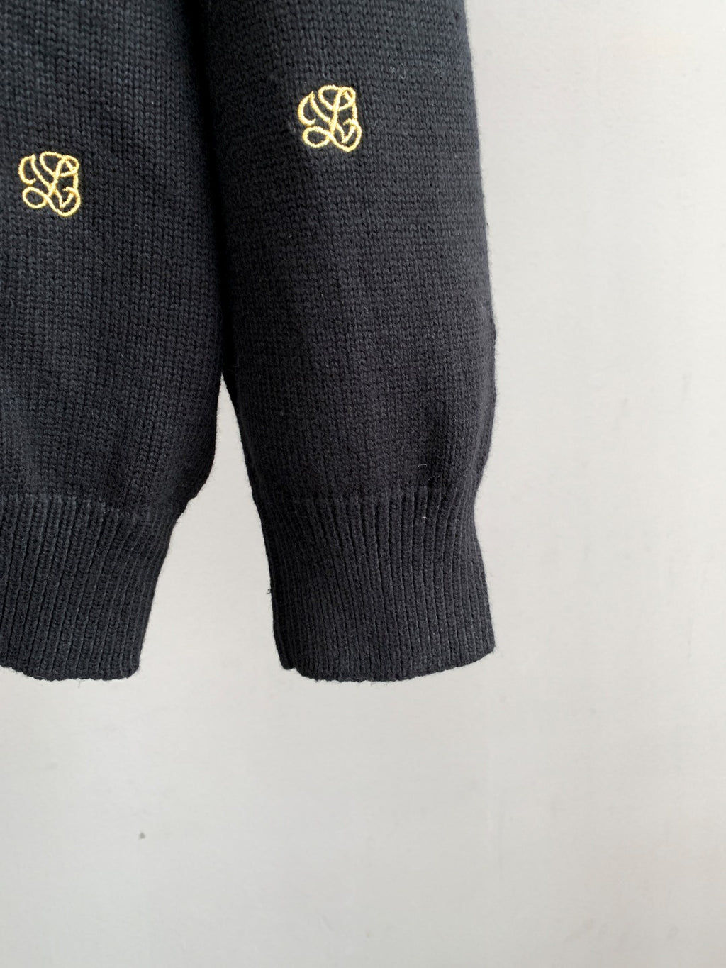 Lower sleeves and ribbed hem of dark knit cardigan with gold monogram details