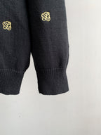 Lower sleeves and ribbed hem of dark knit cardigan with gold monogram details