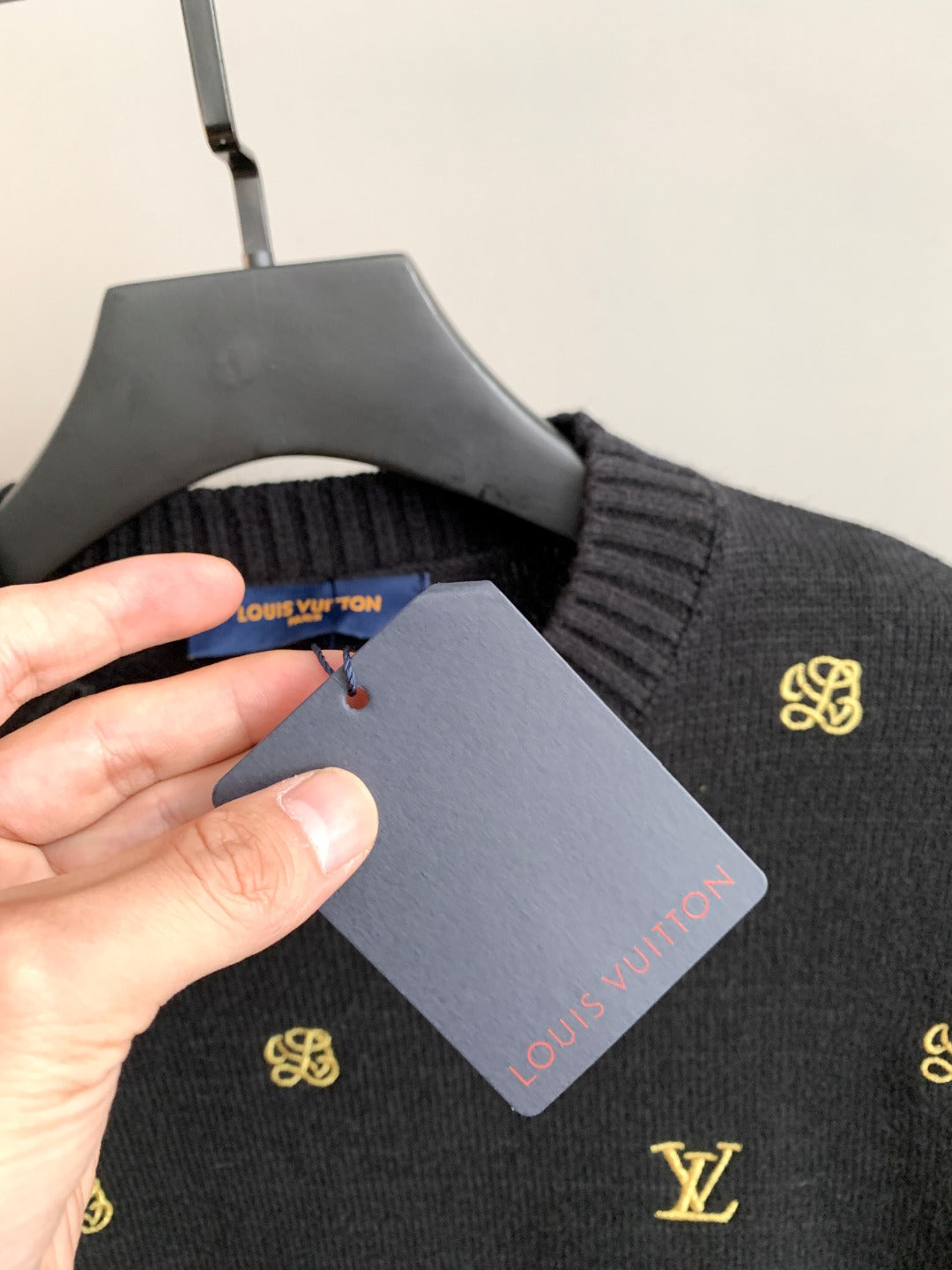 Dark knit sweater collar with gold emblem, tag held by hand.