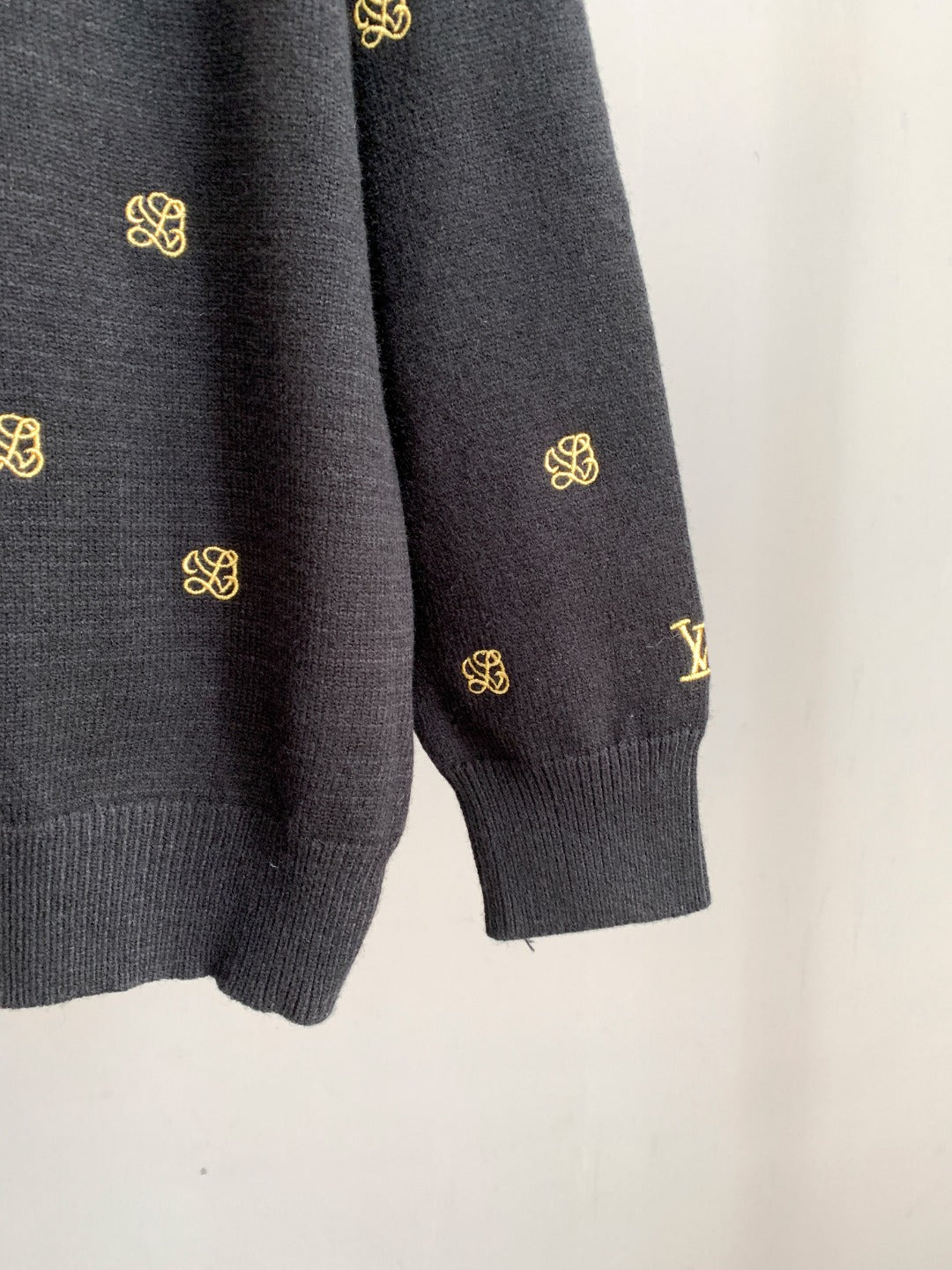 Dark knit sweater sleeve cuff with gold monogram pattern.