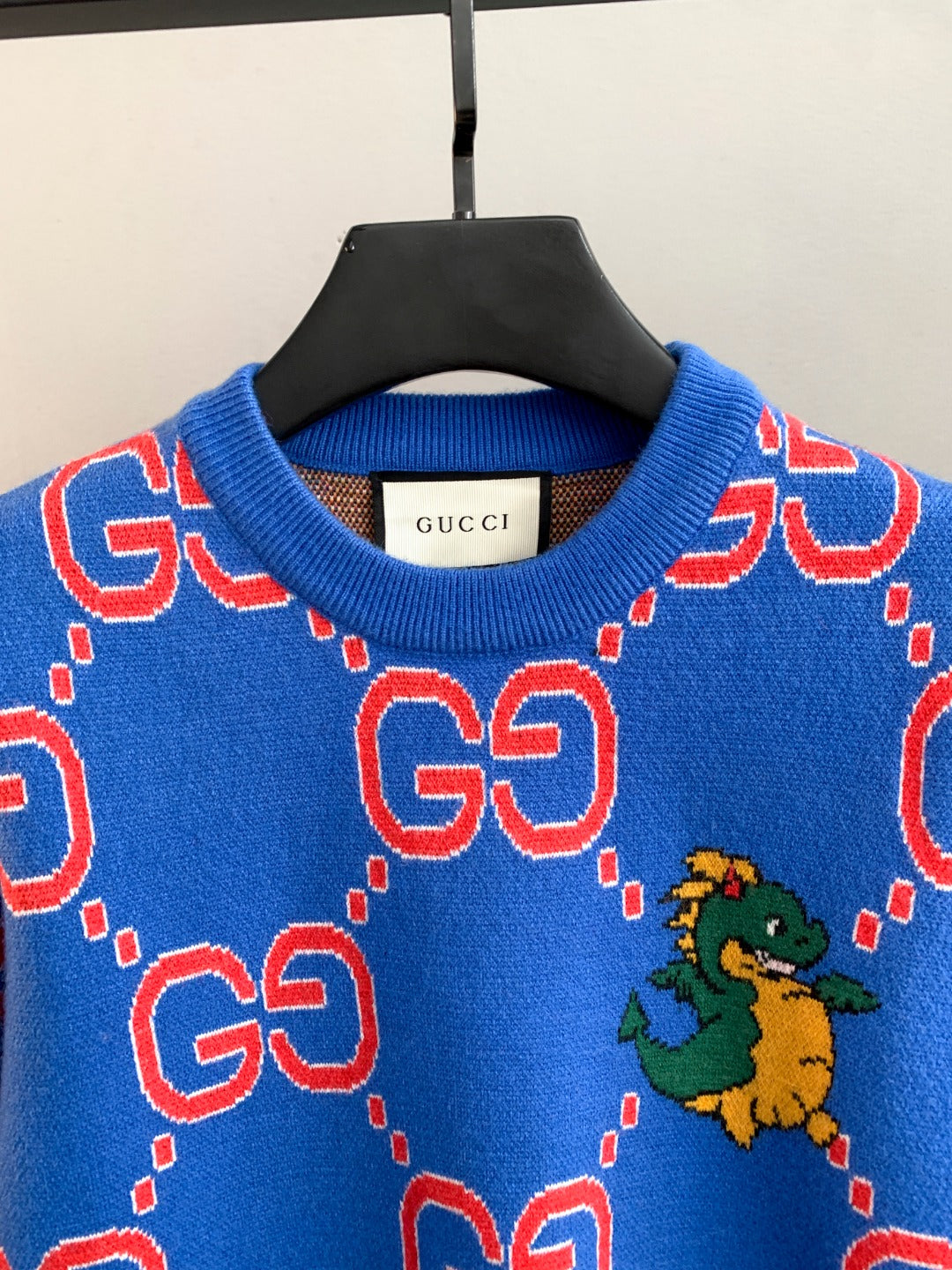 Blue knit sweater neckline with red GG logo shapes and a small green dragon graphic