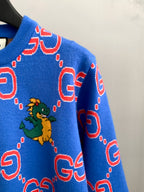 Blue knit sweater sleeve with red GG pattern and small green dragon graphic