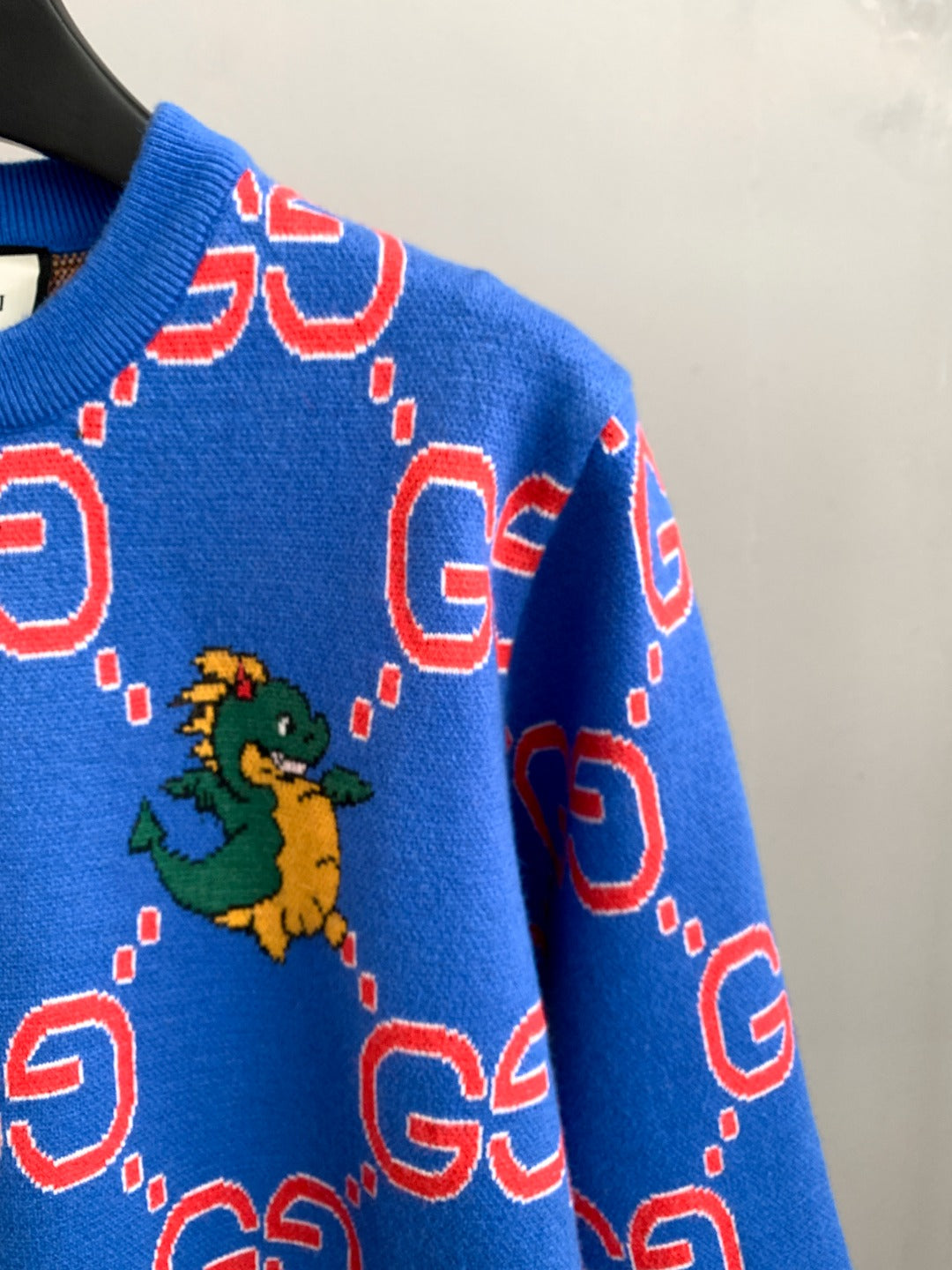 Blue knit sweater sleeve with red GG pattern and small green dragon graphic
