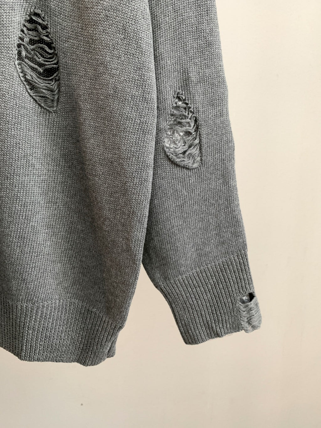 Gray knit sweater sleeve with ribbed cuff and small embroidered motif