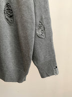 Gray knit sweater sleeve with ribbed cuff and small embroidered motif