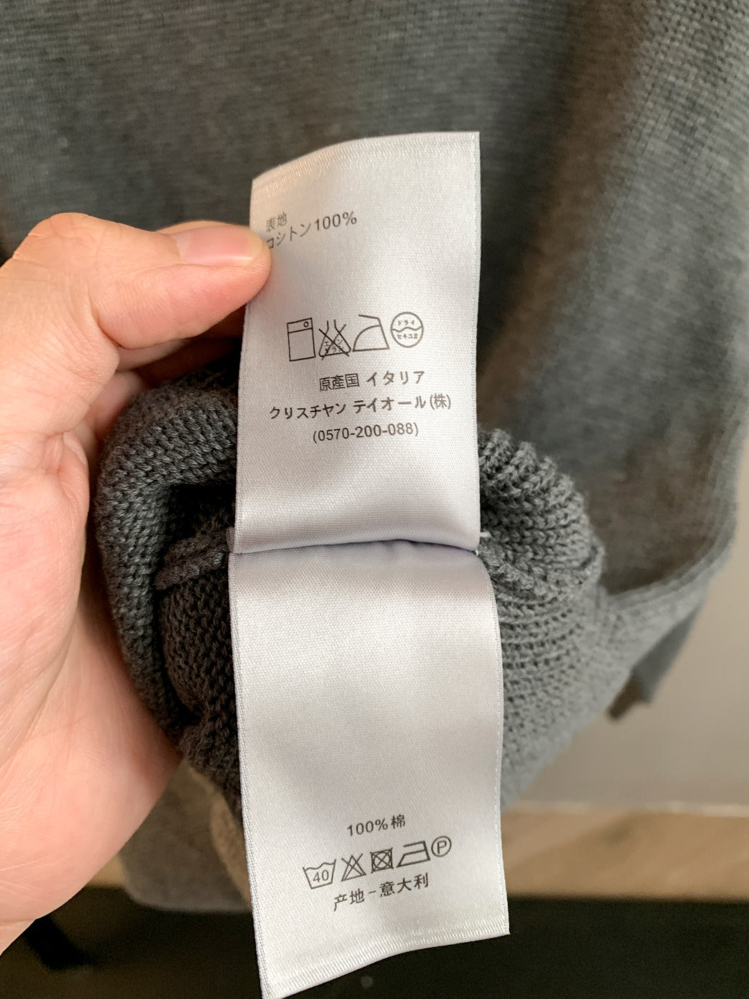 Gray knit sweater care label on inside collar area, held by hand
