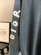 Gray knit sweater sleeve with embroidered whale-like icon and ribbed cuff