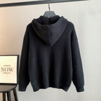 Back view of a dark hooded knit sweater with draped hood and ribbed cuffs