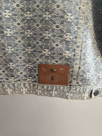 Close-up of gray embroidered jacket hem with brown brand patch and metal button